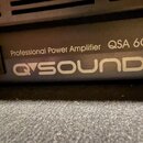Detailní záběr na přední panel černého zesilovače. Je na něm bílý nápis Professional Power Amplifier QSA 600 a pod ním logo QSOUND. Vlevo je vidět vy…