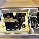 Kytarový pedál v krabici s polystyrenovými vložkami a přiloženým napájecím adaptérem. Na zařízení je bílý nápis VINTAGE TUBE MONSTER VACUUM TUBE OVER…