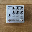 Stříbrný efektový pedál s nápisem GOLDEN MASTER PEDAL a doplňkovým textem 24 BIT 96 KHZ. Zařízení má několik otočných potenciometrů s popisky VU IN O…