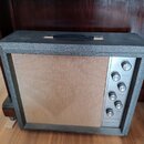 Kytarový zesilovač v šedém texturovaném potahu s béžovou mřížkou. Na pravé straně je kovový ovládací panel s knoflíky a nápisy MICROPHONE, INSTRUMENT…