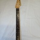 Fotografie zobrazuje krk elektrické kytary s hřístidlem z tmavého dřeva a světlou hlavou. Na hlavě je viditelné logo Fender a nápisy STRATOCASTER a M…