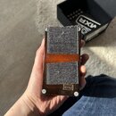 Ruka drží kytarový efekt v hnědém provedení s dvěma šedými textilními pásy na horní straně. V dolní části je vidět malý nápis MXR. Vedle efektu je um…
