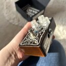Kytarový efekt v hnědém kovovém šasi s bílým ornamentálním vzorem na horní straně. Na přístroji jsou tři průhledné plastové knoflíky a jeden přepínač…