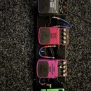 Na černém pedalboardu jsou umístěny čtyři efektové pedály propojené modrými kabely. Horní černý pedal je ladič s nápisy „CHROMATIC TUNER TU300“ a log…