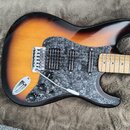 Elektrická kytara s tělem v provedení sunburst a hnědým perleťovým pickguardem. Nástroj má tři snímače, pětipositionní přepínač a tři ovládací knoflí…