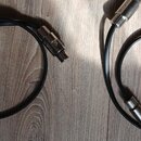 Dvě černé audio kabeláže s kovovými konektory. Na kovových částech konektorů je vyražen nápis "NEUTRIK". Kabely jsou svinuté do kruhu a položené na d…
