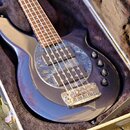 Tmavě modrá elektrická basová kytara v otevřeném kufru s hnědým polstrováním. Nástroj má perleťový pickguard, dva snímače a tři ovládací knoflíky. Na…