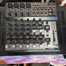 Šedý mixovací pult značky behringer s nápisem XENYX. Zařízení obsahuje několik vstupních kanálů s potenciometry pro GAIN, EQ a LEVEL, červené tlačítk…