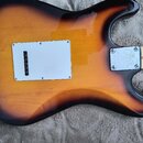Zadní strana elektrické kytary s povrchovou úpravou sunburst. Na těle je vidět stříbrný kovový kryt elektroniky a u krku kovová spojovací deska s náp…