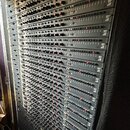 Fotografie zachycuje velký rack s mnoha vnořenými moduly zvukového vybavení v tmavé barvě. Na pravém okraji jednotlivých modulů je opakovaně viditeln…