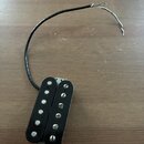 Černý humbucker s dvěma řadami magnetických pólů. Nástroj nemá žádné viditelné značky ani nápisy. Z těla vychází černý kabel s odhalenými barevnými v…