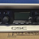 Stříbrný rackový výkonový zesilovač s černým předním panelem. Na panelu jsou nápisy GXD 8, PROCESSING AMPLIFIER a logo QSC. Jsou zde dva ovratidla s…