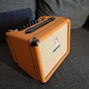 Kytarový kombozesilovač v oranžovém vinylu s béžovou textilní maskou. Na přední straně je umístěn bílý obdélníkový štítek s nápisem ORRIDGE a nad ním…