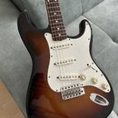 Elektrická kytara s trupem v tmavě hnědé barvě s přechodem do světlejší středu (sunburst) a bílým pickguardem. Nástroj má tři bílé snímače, tři ovlád…