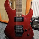 Elektrokytara s červeným metalickým povrchem těla a hnedým hmatníkem. Je vybavena dvěma černými humbuckery a černým tremolo mostem. Na těle jsou dva…
