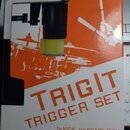 Fotografie znázorňuje krabici s produktem TRIGIT TRIGGER SET. Na obalu je zobrazen černý trigger se žlutým gumovým hrotem a grafika bubeníka u bicích…