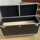 Otevřený černý transportní case s hliníkovými hranami a vršnicemi. Vnitřní stěny jsou vyloženy černou textilií a dno je z nebarveného dřeva. Na předn…
