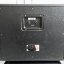 Zadní strana černého kytarového reproduktoru potaženého texturovaným vinylen. V horní části je panel se dvěma vstupy označenými nápisy INPUT a THROUG…