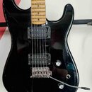 Černá elektrická kytara s lesklým povrchem a hnedým javorovým hmatníkem. Nástroj má dva humbuckery s černými kryty, dva oválné ovládací knofíky a tre…