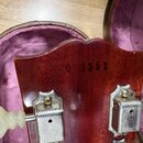 Detail zadní strany hlavy kytary z červeného dřeva. Uprostřed je vyryjeno číslo 0 1952. Jsou vidět dva kovové ladičky s bílými plastovými knoflíky. P…