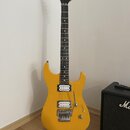 Žlutá elektrická kytara s tmavým hnedým hmatníkem a bílými tečkovanými značkami. Na hlavě je viditelné logo Jackson. Kytara má dva humbuckery, tremol…