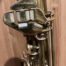Detailní záběr na mechanismus klavíš saxofonu v mosazném provedení. Jsou vidět bílé plasty na klavíších a viditelné opotřebení povrchu v podobě škráb…