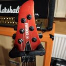 Fotografie zachycuje hlavu červené elektrické basy v černém stojanu. Na hlavě je svisle umístěn bílý nápis YAMAHA a pod ním logo značky. V pozadí je…