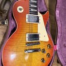Elektrická kytara s trupem v barvě sunburst a viditelnou strukturou dřeva, umístěná v otevřeném kufru s fialovou výstuhou. Nástroj má dva humbuckery…