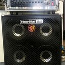Fotografie zobrazuje basový zesilovač v racku umístěný na basové reproducing Hartke HD410. Na zesilovači je vidět logo GW a nápis 750x Professional B…