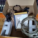 V kartonové krabici s bílým polystyrenem je sada příslušenství. Obsahuje napájecí adaptér, kabel s několika konektory, smotaný stříbrný kabel a krouž…