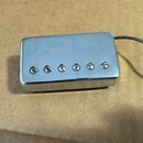 Stříbrný humbucker s kovovým krytem a šesti viditelnými šrouby v řadě. Z pravé strany vychází opletený šedý kabel. Povrch krytu vykazuje drobné škráb…