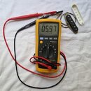 Fotografie zobrazuje žlutý digitální multimetr značky MASTECH model MS8217, který měří odpor na černém elektrickém snímači kytary. Na displeji přístr…