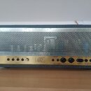 Zadní strana šedého zesilovače s perforovaným kovovým krytem. Na spodním panelu jsou různé přepínače a konektory s nápisy: POWER SWITCH, FX LOOP (SEN…