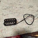Černý humbucker s dvěma řadami bílých pólů. Na spodní části je bílý nápis Seymour Duncan. Snímač má připojený černý kabel s odhalenými vodiči v koncí…
