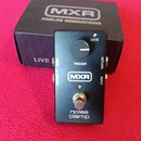 Černý efekt pedál s nápisy MXR a noise clamp. Na horní straně je ovládací knoflík, kontrolka s nápisem GATE a přepínač TRIGGER. Na bocích jsou vidite…