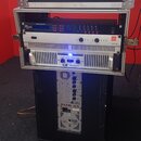 Otevřený hliníkový transportní case obsahuje tři rackové jednotky. Horní zařízení má nápis "v-racks" a "DS", prostřední jednotka nápis "zm5 AMP 1200"…
