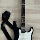 Černá elektrická kytara typu Stratocaster s bílým pickguardem a hnedým hmatníkem. Na hlavě je nápis Fender. Kytara má tři snímače typu single-coil, b…