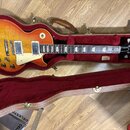 Elektrická kytara s trupem v žlutě-oranžovém sunburst provedení a bílým pickguardem leží v hnědém tvrdém kufru s červenou výstuhou. Na hlavě kytary j…