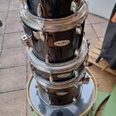 Sada černých bubnů značky MAPEX naskládaných na sebe. Na každém z horních čtyř korpusů je viditelné oválné logo MAPEX. Dole je umístěn největší buben…