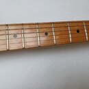 Detail hředu kytary s dřevěným hmatníkem světle hnědé barvy. Na hmatníku jsou vidět kovové pražce a tři kulaté tmavé polohové značky. Povrch dřeva vy…