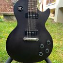 Černá elektrická kytara s matným povrchem a dvěma humbuckery. Na přepínači tónů jsou viditelné nápisy RHYTHM a TREBLE. Nástroj má čtyři ovládací knof…
