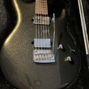 Elektrická kytara s tmavě šedým metalizovaným povrchem v černém pouzdře. Nástroj má dva snímače typu humbucker, jeden ovladač hlasitosti, jeden tón a…