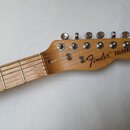 Hlava a hриф elektrické kytary z přírodního dřeva. Na hlavě je černé logo Fender a nápis TELECASTER. Jsou zde vidět šest ladicích kolíčků a kovový pr…