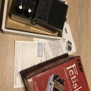 Černý kytarový efekt s nápisem Fetish a podtitulem FET OVERDRIVE TECHNOLOGY. Na přístroji jsou tři ovládací knofíky s popisky LEVEL, GAIN a FAT, červ…