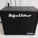 Černý kytarový reproduktor v koženém potahu s černou textilní mřížkou. Uprostřed je bílý nápis Hughes & Kettner a v pravém dolním rohu štítek s nápis…