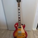 Elektrická kytara s trupem v červeno-žlutém sunburst provedení a krčkem z tmavého dřeva. Na hlavě je bílý nápis Epiphone a pod ním kurzivní nápis Les…