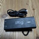 Černý obdélníkový interface s nápisem iRig a označením HD 2. Na povrchu jsou vidět drobné škrábance a prach. Vedle zařízení leží černý USB kabel.