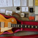 Elektrická kytara s žlutým lakem a hnědým hmatníkem v otevřeném červeném tvrdém pouzdře. Na hlavě kytary je viditelné logo Gibson. K nástroji je přil…