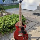 Červená elektrická kytara s tmavě hnědým hmatníkem a černým pickguardem. Na hlavě je bílý nápis Gibson a pod ním kurzivní nápis Les Paul. Nástroj je…