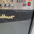 Detail ovládacího panelu a části membrány kytarového komba. Na stříbrném panelu je nápis ATTAX 100, čtyři otočné ovladače s popisky MASTER, REVERB, F…